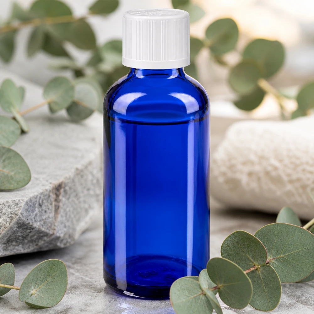 Farmaceutisch glazen flesje van 50 ml in blauw met een KiSi-dop, omringd door verse eucalyptusblaadjes
