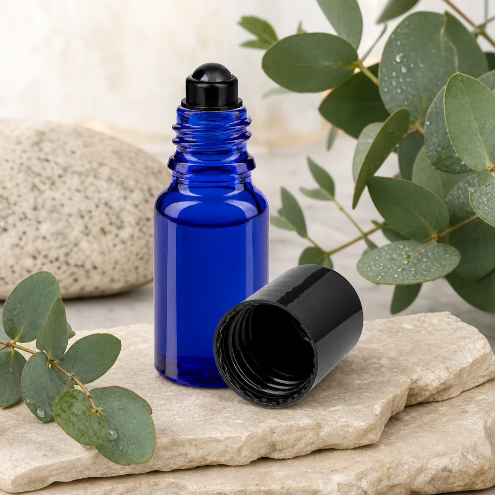 Aromatherapie-roll-onflesje van 10 ml, kobaltblauw met zwarte dop, op lichte kalksteen met groene planten