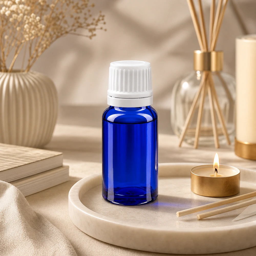 Blauwe glazen flessen 10ml met wit 1.2mm druppelstop OV Kobaltblauw ApoGlas-flesje van 10 ml met witte buitenverpakking naast een rietdiffuser en een geurkaars