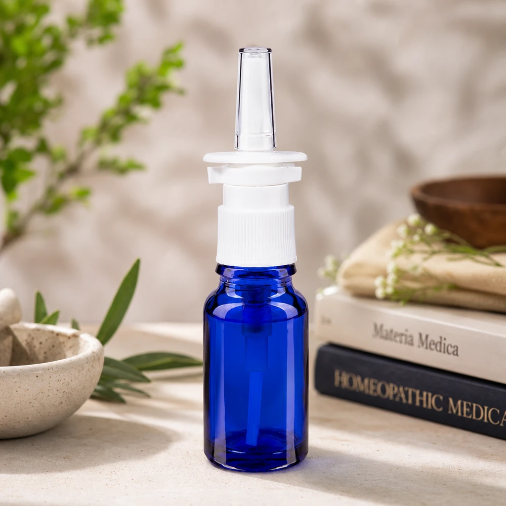 Blauwe glazen flessen 10ml met neusverstuiver Blauw glazen flesje van 10 ml met neusspraykopje naast een vijzel en groene kruidentakjes