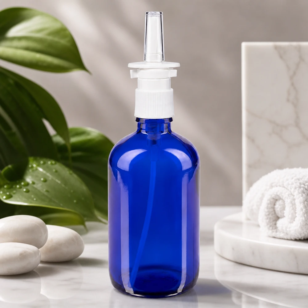 Blauwe glazen flessen 100ml met neusverstuiver Blauwe glazen neussprayfles van 100 ml met doorzichtige applicatordop, afgebeeld tegen een achtergrond van tropische bladeren