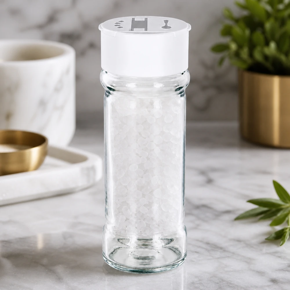 Zout-/kruidenpotje 100 ml met dubbele strooier, wit Doorzichtig kruidenpotje van 100 ml met een witte dubbele strooier op marmer, gevuld met grof zeezout