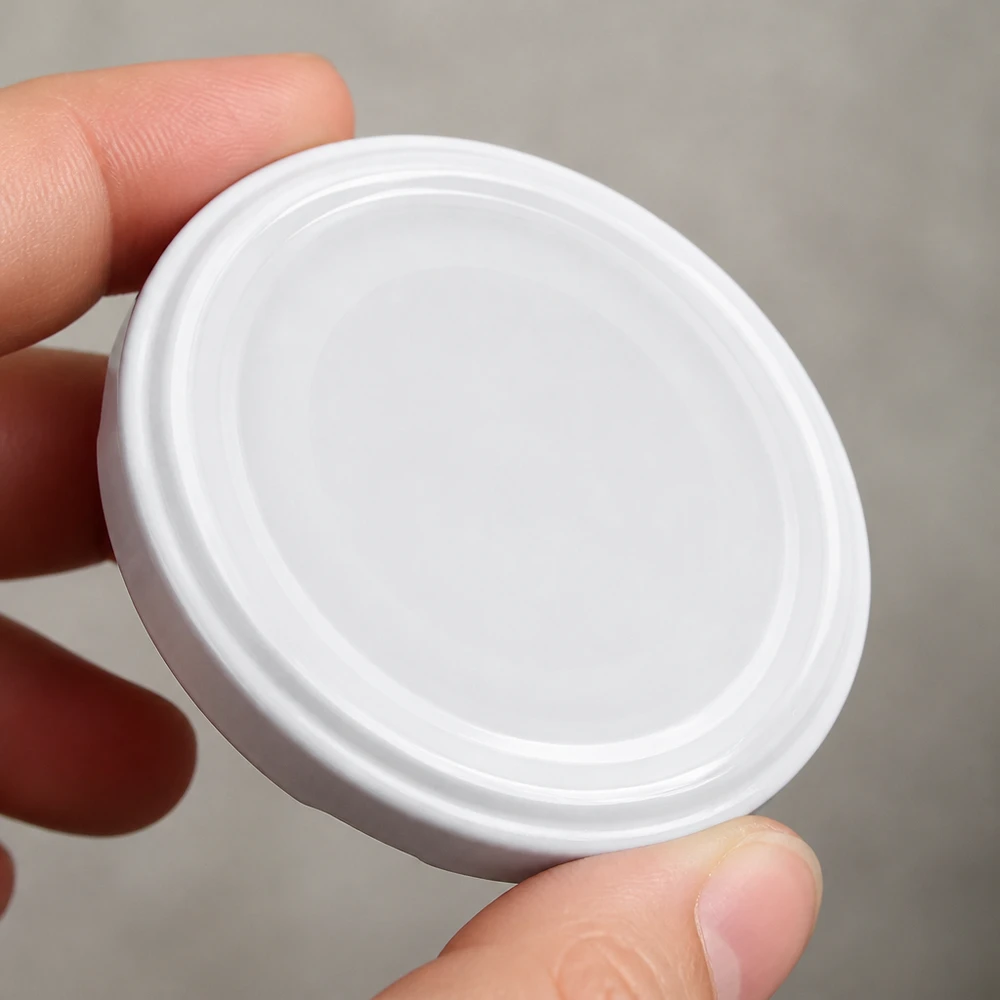 82mm BioSeal deksel wit (TO82) UNiTWIST UNiTWIST TO82 wit BioSeal-blikdeksel tussen de vingers gehouden – detailbeeld