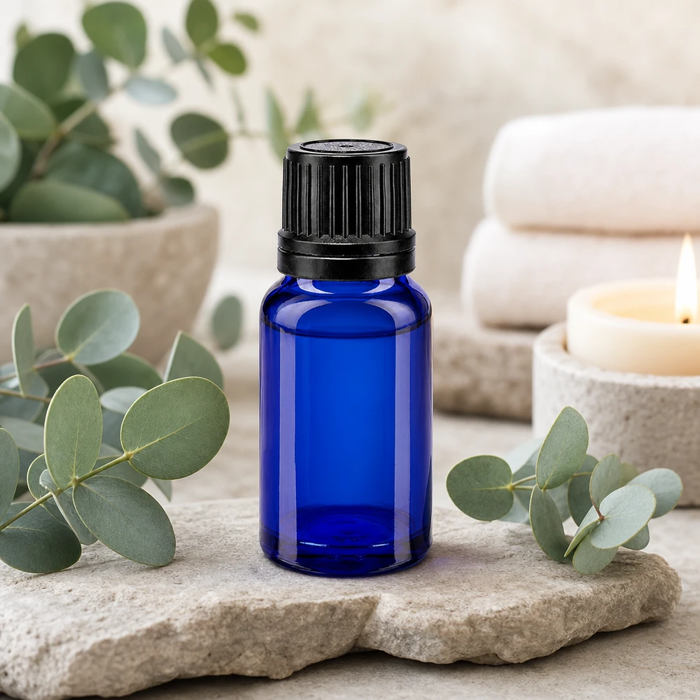 Blauwe glazen flessen 10ml met zwart sluiting OV gietring Een blauw glazen flesje van 10 ml met een zwarte dop, omringd door eucalyptus en wellness-accessoires