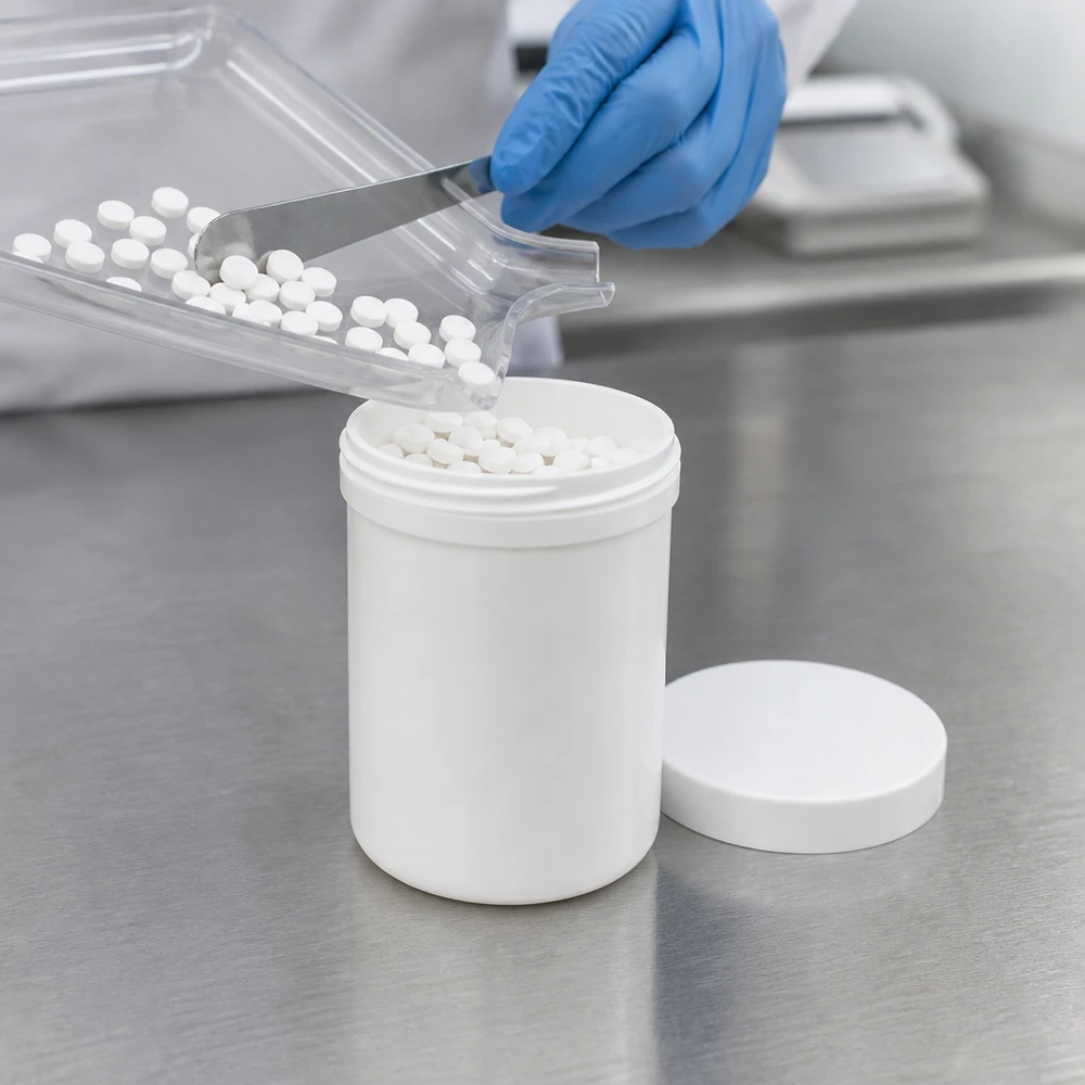 Een witte pot van 150 g, gemaakt van PP, waarvan de schroefdop is verwijderd, wordt gevuld met witte tabletten