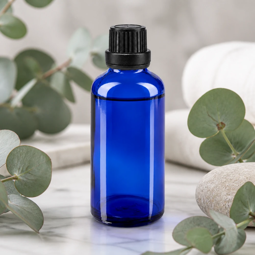 Farmaceutische druppelfles van 50 ml in blauw met OV-sluiting, omringd door eucalyptusbladeren en steentjes