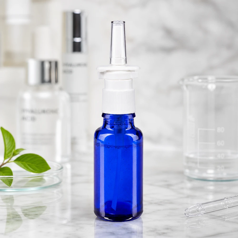 Blauw apothekersflesje van 20 ml met neusspraykop, omringd door laboratoriumbenodigdheden en een plantenblad