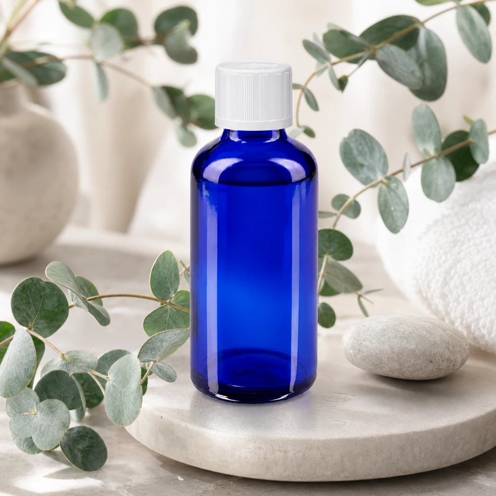 Cilindrische blauwe glazen fles van 50 ml met een witte kindveilige sluiting en een natuurlijke decoratie
