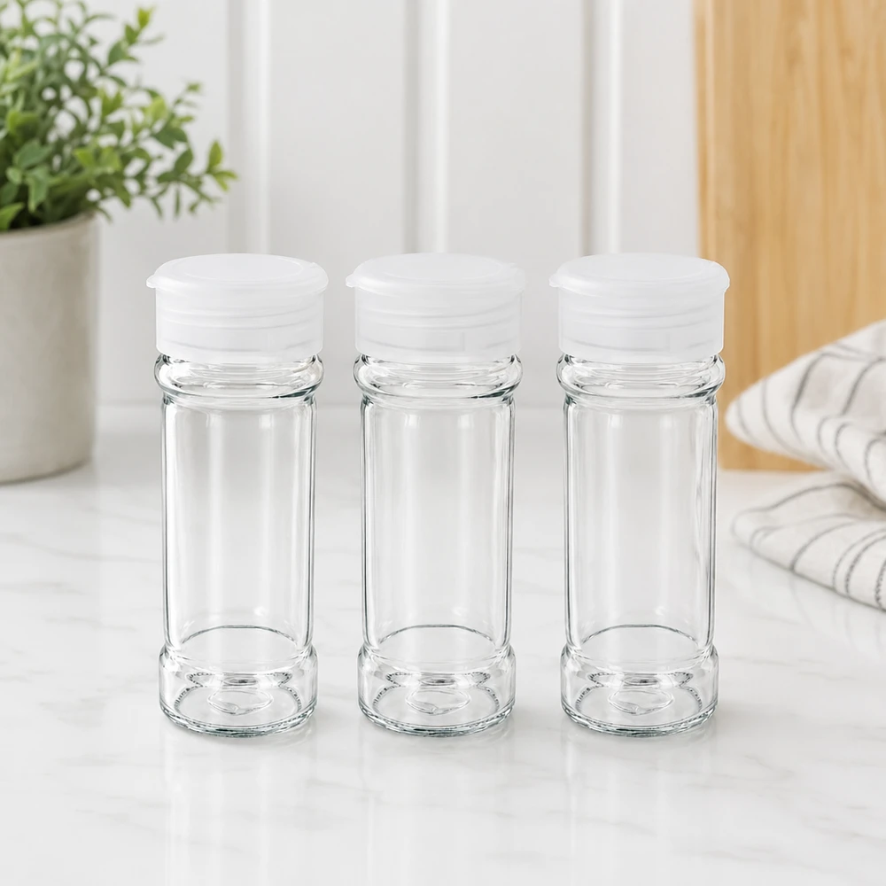 Drie lege, doorzichtige kruidenpotjes van 100 ml met witte strooideksels op een marmeren ondergrond
