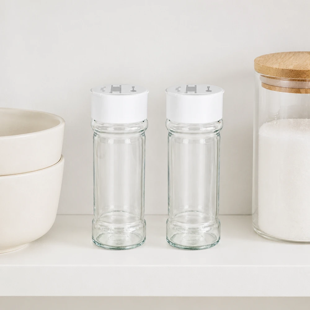 Twee kruidenpotjes van 100 ml met een witte deksel met dubbele strooier, naast elkaar op een witte plank