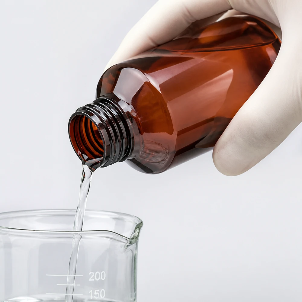 PET fles 100ml PP28 zonder dop Doseren van laboratoriumvloeistof uit een bruine PET-fles met smalle hals van 100 ml in een bekerglas met schaalverdeling