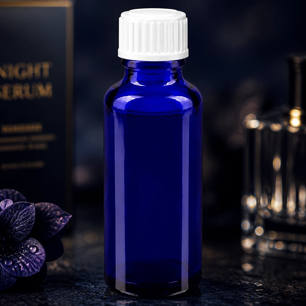 Cilindrische blauwe glazen fles van 30 ml met een witte schroefdop op een donkere achtergrond met bloemen