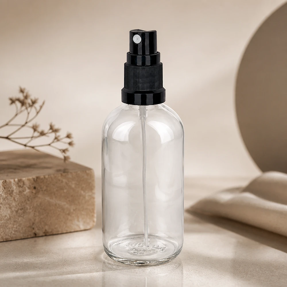 Minimalistisch vormgegeven verstuiver van 100 ml van helder glas met een zwarte verstuiver op marmer