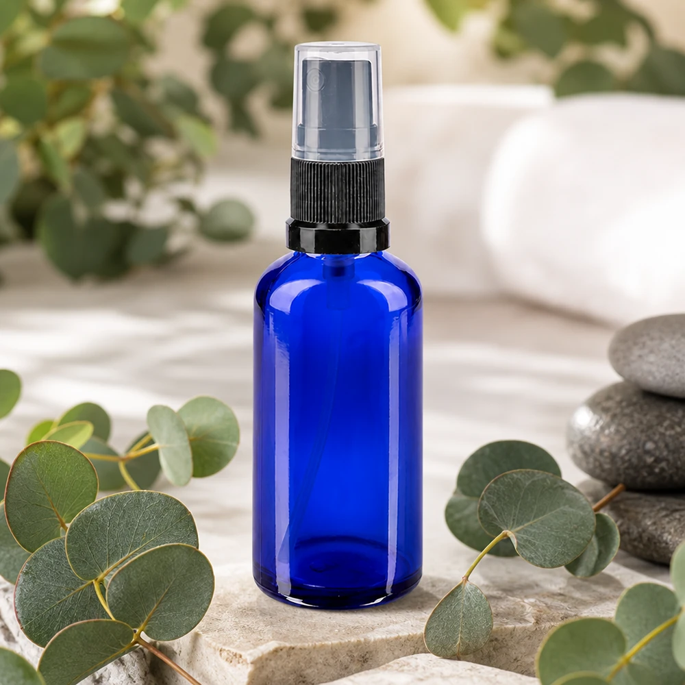 Blauwe glazen spuitfles van 50 ml met een zwart pompmechanisme tussen eucalyptustakjes