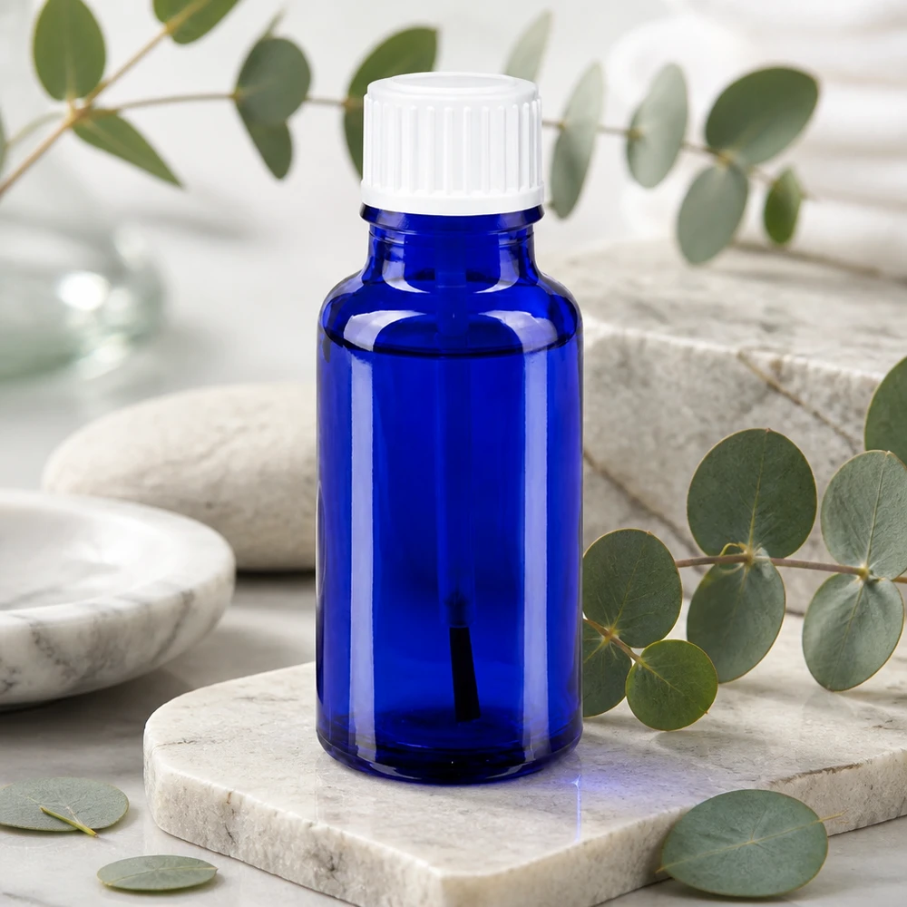 Blauw glazen flesje van 20 ml met een witte dop, omringd door natuurstenen en eucalyptus