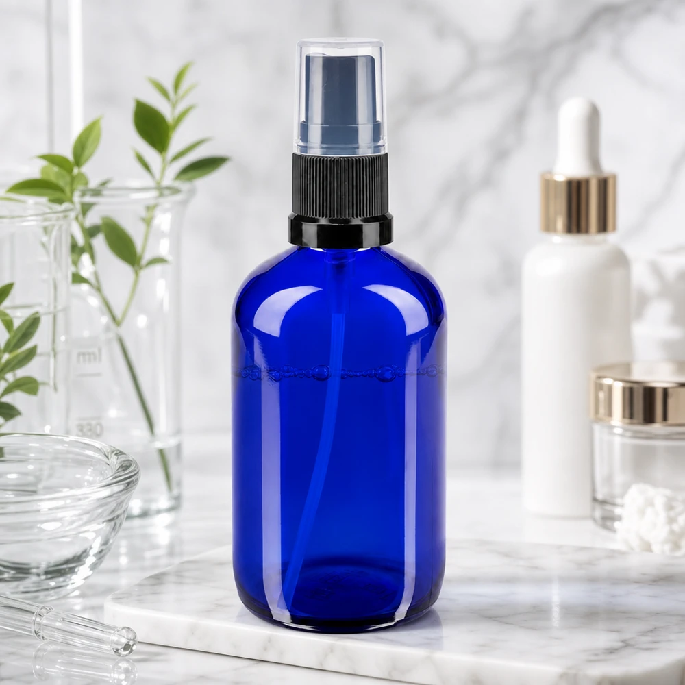 Blauwe glazen spuitfles van 100 ml STD met zwarte spuitkop naast een serum- en crèmepotje op marmer