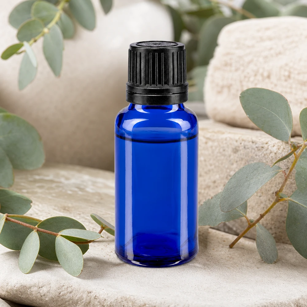 Blauwe glazen flessen 20ml met wit druppelsluiting 1mm VR Kleine blauwe glazen fles met druppeldispenser van 20 ml, omringd door eucalyptus op een stenen achtergrond