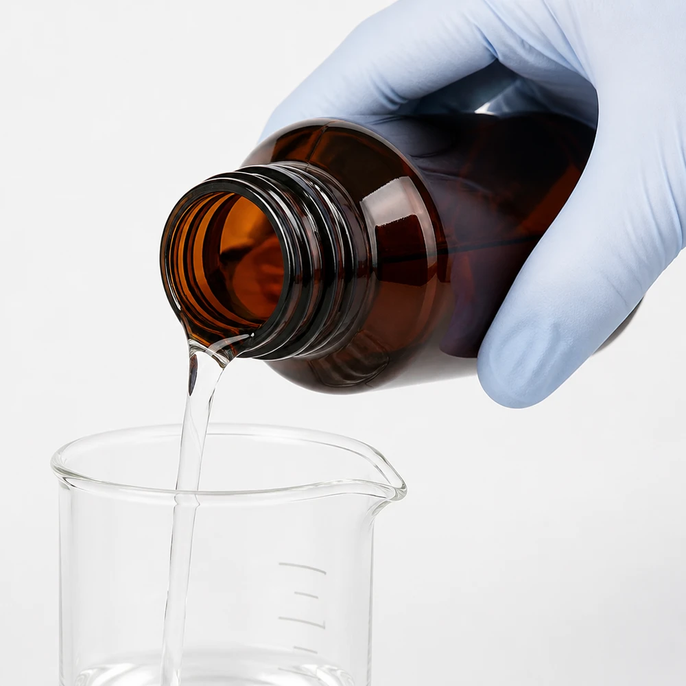 Klare Flüssigkeit wird aus brauner Schraubverschlussflasche in transparentes Laborglas gegossen