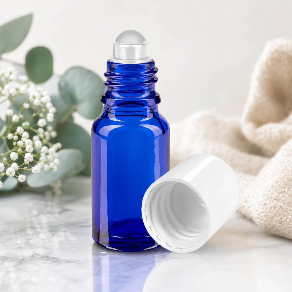 Apothekersflesje blauw 10ml roll-on cap wit Geopende blauwe roll-on-fles van 10 ml met kogelafsluiting, tussen natuurlijke bloemen en een linnen doek