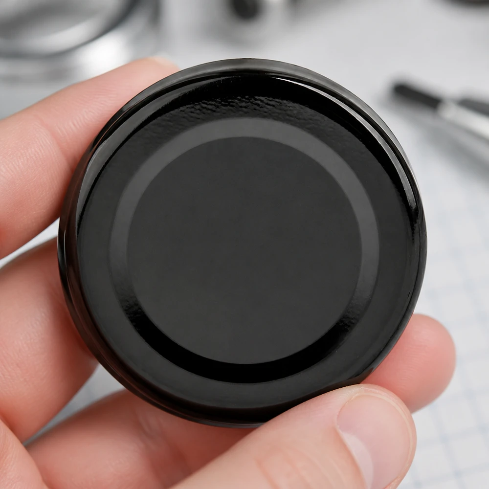 Compacte zwarte BasicSeal-deksel TO43 UNiTWIST van 43 mm tussen duim en vingers