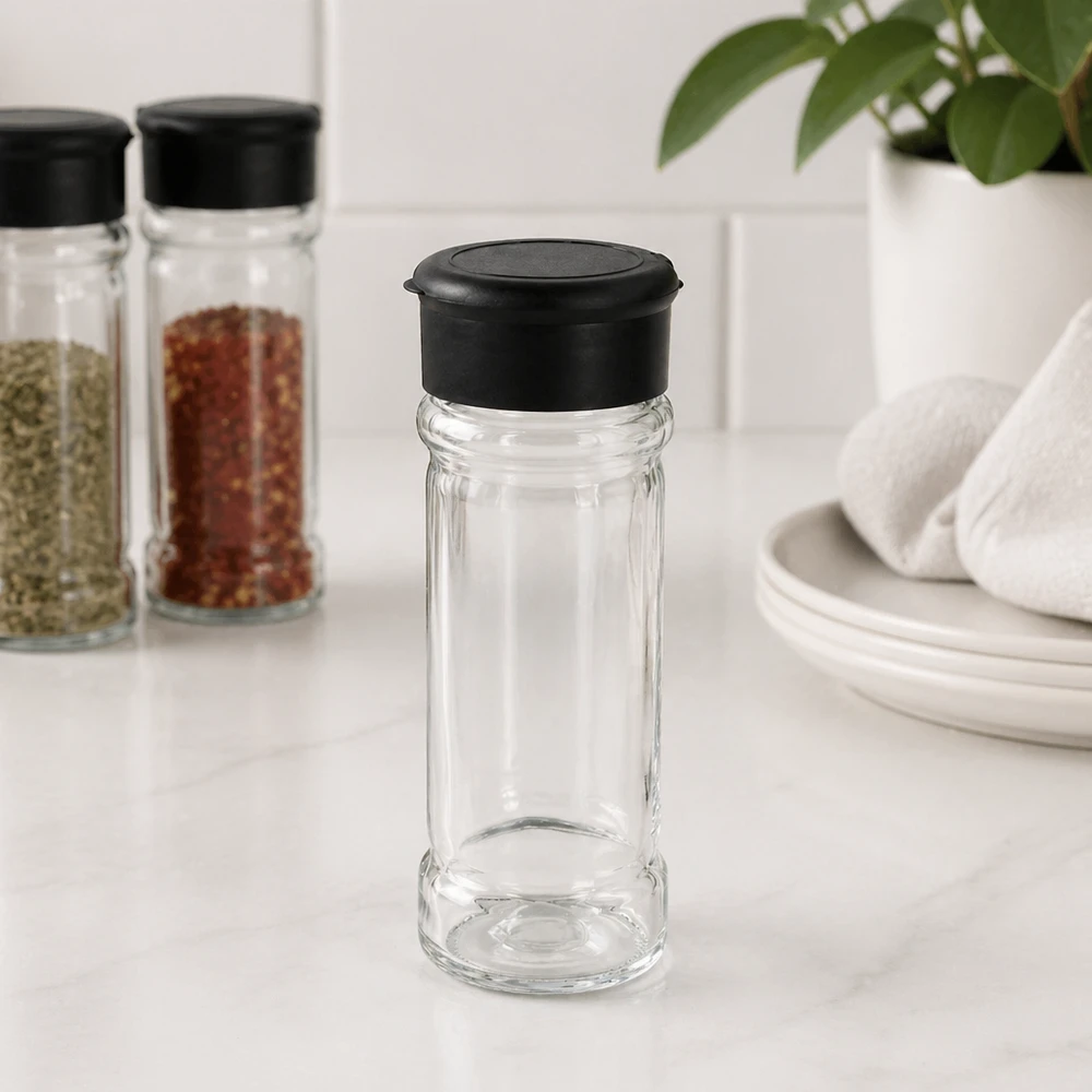Cilindrische kruidenstrooier van helder glas met een zwart deksel in een moderne keukenomgeving