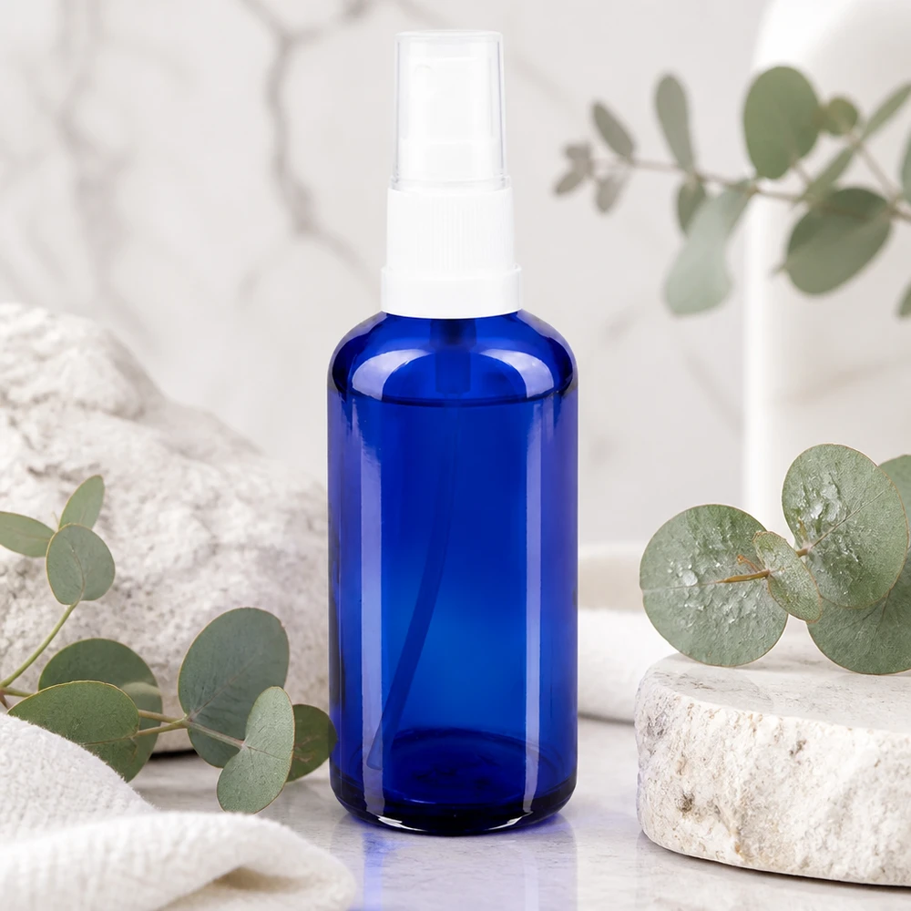 Blauwe glazen flessen 50ml met wit pompverstuiver Blauwe glazen spuitfles van 50 ml met witte verstuiver op marmer met eucalyptus