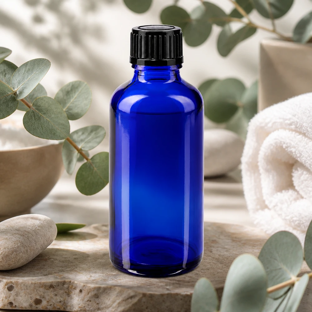 Kleine blauwe glazen flesje van 50 ml voor etherische oliën, met een zwarte dop en eucalyptustakjes