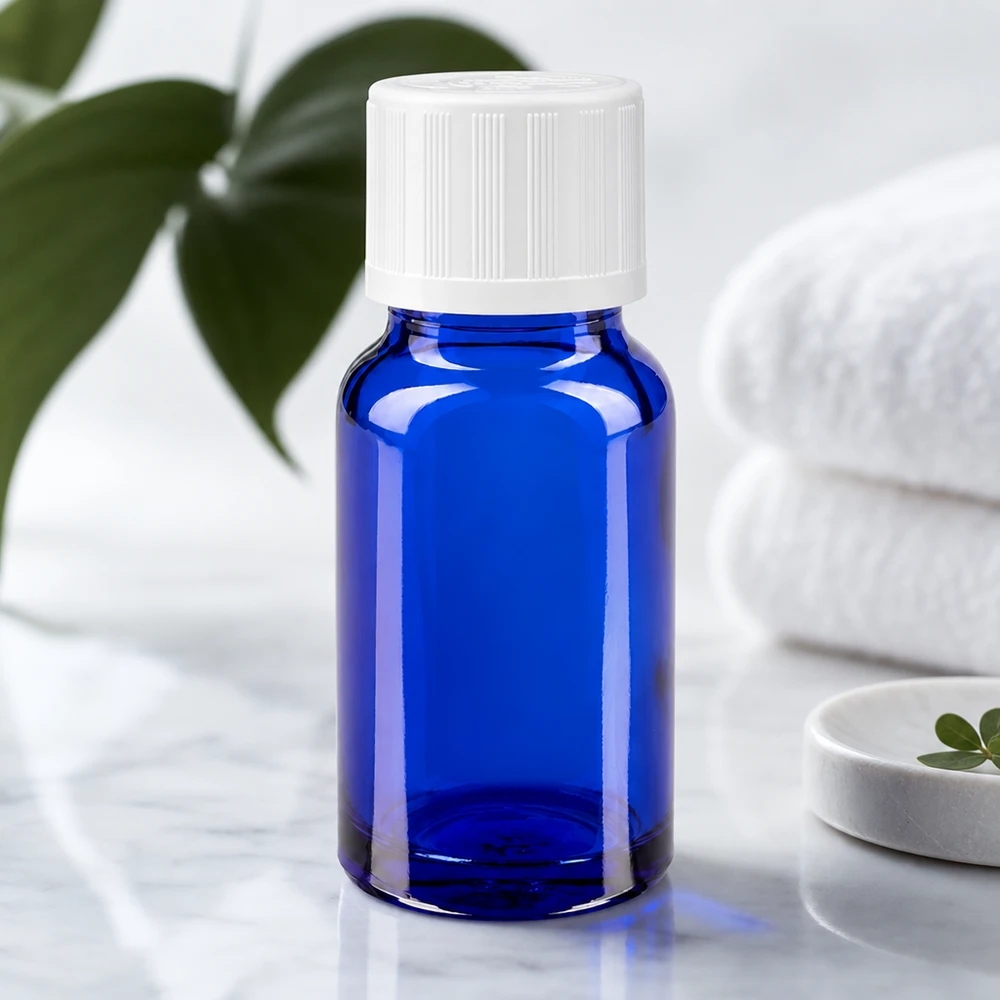 Kleine kobaltblauwe apothekersfles met een witte druppeldop naast groene bladeren