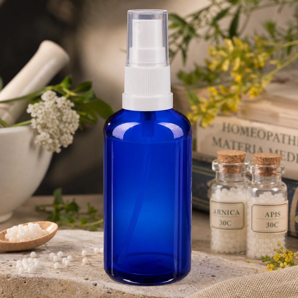 Blauwe glazen apothekerssprayfles van 50 ml met witte pompkop, naast homeopathische globuli